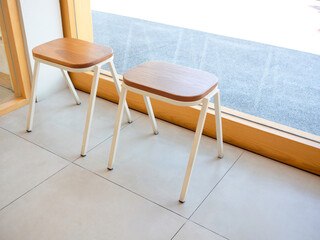 Empty two small wooden chairs without backrest near the glass wall inside the coffee shop. Customer...