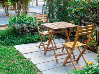 Outdoor garden table set. Empty wooden table and two chairs on concrete floor on green grass in the park, nobody.