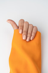 A close shot of a thin graceful hand of a girl with a nude manicure holds in an orange jacket on a...