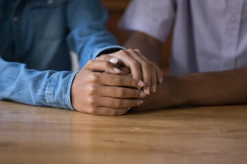 Obraz premium Young African married, dating couple holding arms, touching hands over table, giving empathy, compassion. Wife consoling husband, touching male hands with love, care. Close up, cropped shot