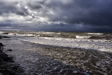 the figure of a lonely man entering a raging sea with big waves against a cloudy sky