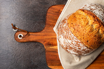Wholemeal sourdough bread on linen napkin on brown wooden chopping board.