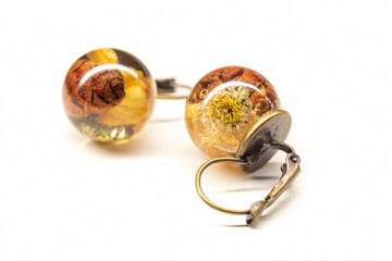 Bronze earrings with epoxy resin. Natural dried chamomille flwoers and small tree cones inside sphere balls. Selective focus on the details, object isolated on white background.