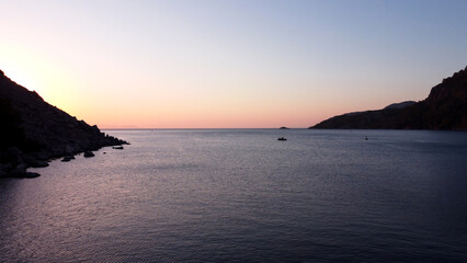 Naklejka premium Sunrise over mountain rock in sea water. Sunrise seascape in calm sea. Rocks silhouette and golden reflections on the rippled water. Aerial drone view.