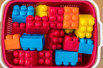 Plastic red basket with colorful toy blocks for children game top close view. Childcare and creative education concept.