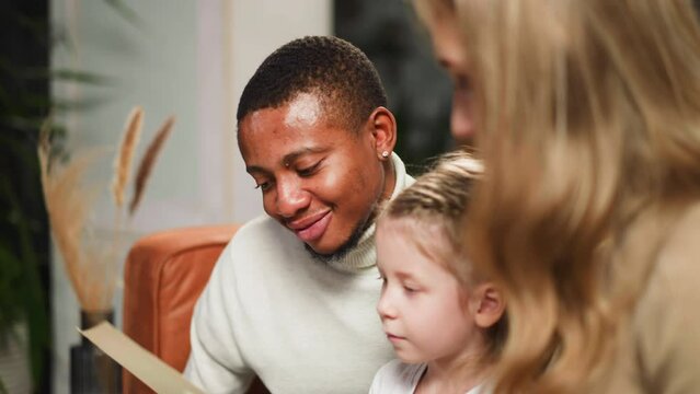 Man nods looking at old pictures with woman and little girl