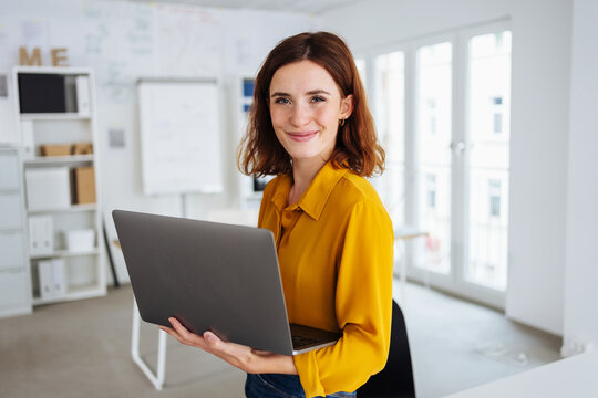 Smiling friendly young business manageress holding a laptop