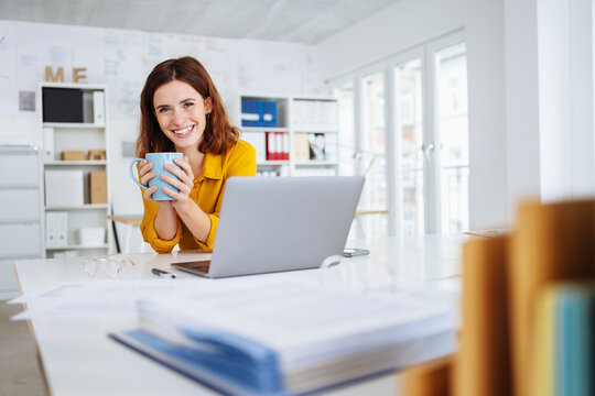 Vivacious happy young businesswoman relaxing over mug of coffee