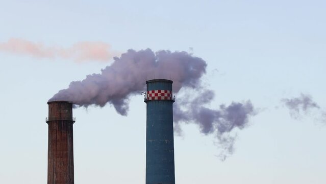 Big factory chimney polluting the atmosphere in sunset light. Thermal power plant chimney shell.