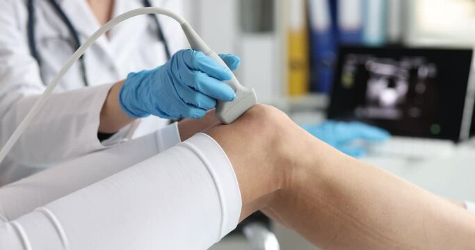 Doctor making ultrasound of knee joint to patient in clinic closeup 4k movie