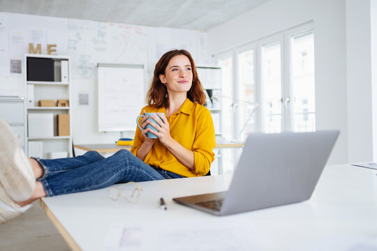 Happy young businesswoman sitting daydreaming in the office