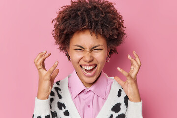Outraged pissed off curly haired woman gestures and screams angrily expresses negative emotions...