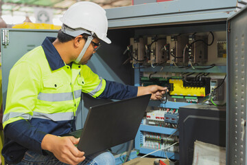 The factory's electrical engineers wear green protective clothing and plastic caps. Use laptops and tablets to check the quality of industrial equipment.
