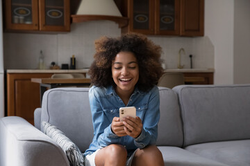 Cheerful happy gen Z teen girl receiving exciting message on smartphone, reading text in screen,...