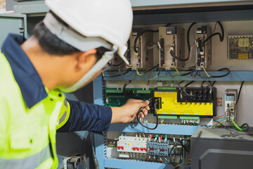 The factory's electrical engineers wear green protective clothing and plastic caps. Use laptops and tablets to check the quality of industrial equipment.
