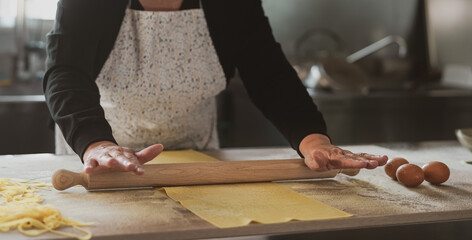 Close up female hands roll the dough preparing fresh homemade pasta