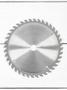 Metal circular saw disc on a white wooden background.