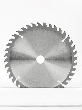 Metal circular saw disc on a white wooden background.