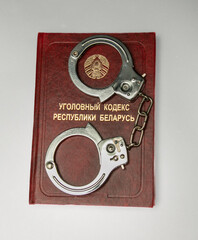 The Criminal Code of the Republic of Belarus and handcuffs on a light background. Translation of the inscription from the Russian language - Criminal Code of the Republic of Belarus. Close-up.
