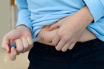 child injecting himself in his stomach. boy teenager patient hand giving insulin pen injection into...
