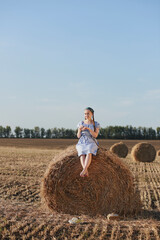 Naklejka na ściany i meble child on hay a girl in a field by a haystack in a blue dress and a scarf with braids