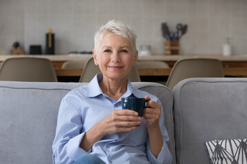 Happy calm carefree middle aged lady enjoying good morning, drinking hot fresh tasty coffee at...