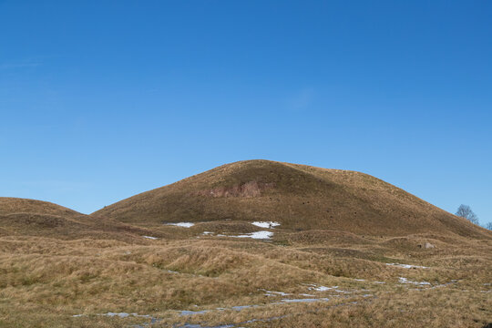 Burial mound covered with grass in rolling hill culture landscape. Patches of snow on the ground