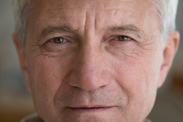 Face of serious mature elder man with brown eyes, wrinkles. Close up front cropped shot of male retiree, senior pensioner looking at camera. Older age, elderly health care concept