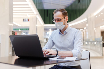 Obraz premium Clerk in face mask man working remotely on laptop in a public place