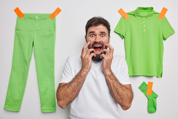 Fearful anxious young man looks embarrassed grabs face keeps mouth widely opened exclaims from...