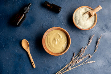 Cosmetic green clay in a wood bowl with aroma oil on a blue background. Natural cosmetic concept.