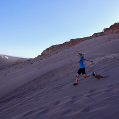 Woman running downhill on sand dune in Atacama desert landscape with blue sky flying sand