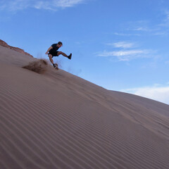 Man jumping and flying downhill on sand dune in Atacama desert landscape with blue sky and flying sand