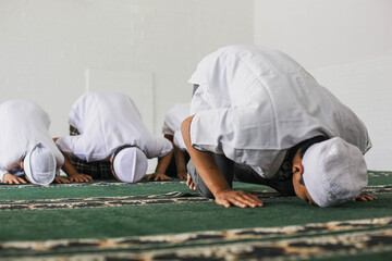 A group of Muslims are praying  in congregation with prostrating movements in the mosque