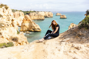 Fototapeta na wymiar young beautiful girl in sits on a rock against the backdrop of the beach and the ocean in Portugal