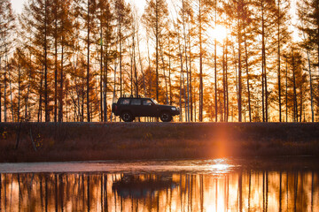 Black SUV on foreat road near a lake at sunset