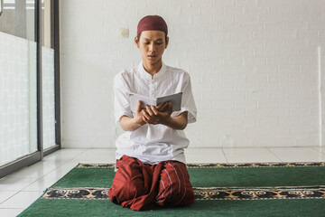 Religious Muslim man sitting on his knees reading the Quran in the mosque