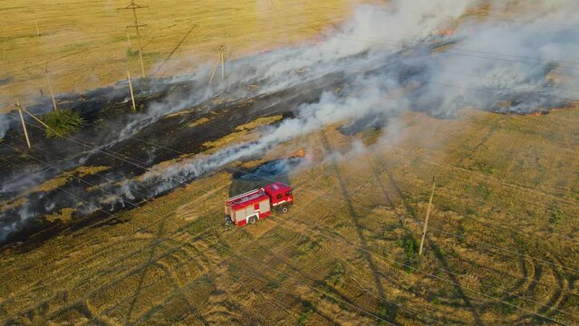 Brave firefighters rush to fight burning flame on agronomic field with clouds of smoke and fire truck with water on danger dry stubble. Emergency case for danger mission and rescue nature saving