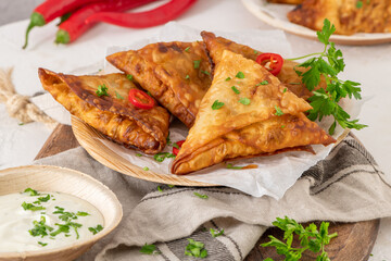 Indian samosas - fried or baked pastry with savoury filling, popular Indian snacks, served with yogurt sauce in areca leaf dishes with spices on kitchen countertop.