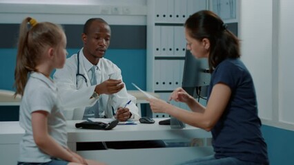 Physician giving prescription document for free medicine to parent after checkup examination in cabinet. Man pediatrician helping small kid and mother with treatment against disease.
