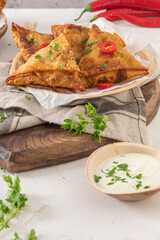 Indian samosas - fried or baked pastry with savoury filling, popular Indian snacks, served with yogurt sauce in areca leaf dishes with spices on kitchen countertop.