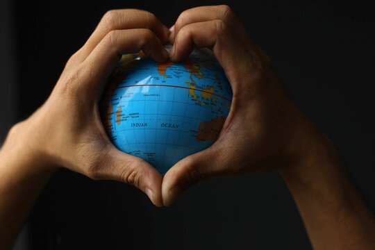 Heart shaped hands holding earth on black background. Earth day concept with low key tone photo