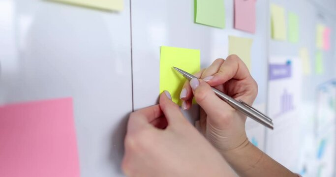Woman manager writes numbers on sticky note on white board closeup