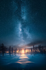 Beautiful sunrise over snowy forest with an epic milky way on the sky