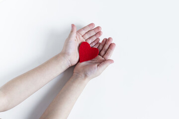 Children's open palms, holding a bright red heart on a light background.