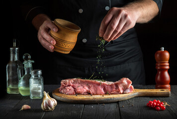 The chef prepares raw veal meat. Before baking, the cook adds dry herbal seasoning to the beef. National dish is being prepared in the kitchen