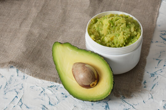 white mockup plastic jar with avocado puree, cut in half avocado and wooden comb