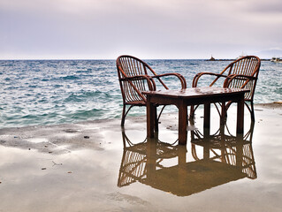 One table and two chairs left on seafront dock during stormy weather. Of season concept.