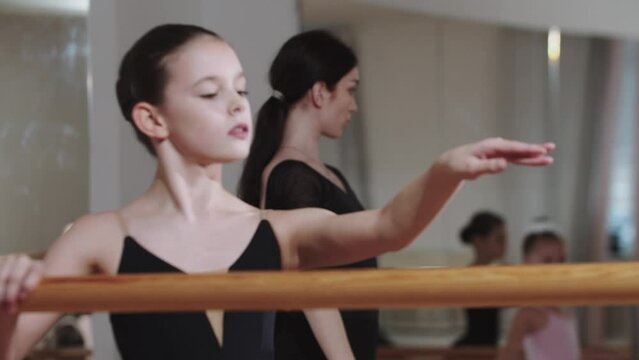Pretty elegant little girl training ballet with group of other girls in the studio