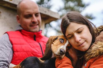 Young couple man and woman male and female playing with their basset hound dog while sitting...
